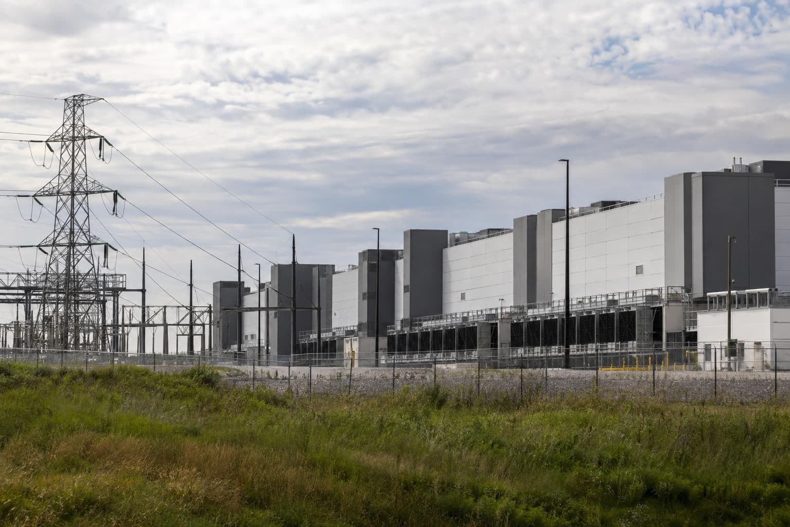 Data-center building beside power lines, illustrating debate over electricity costs and permits.