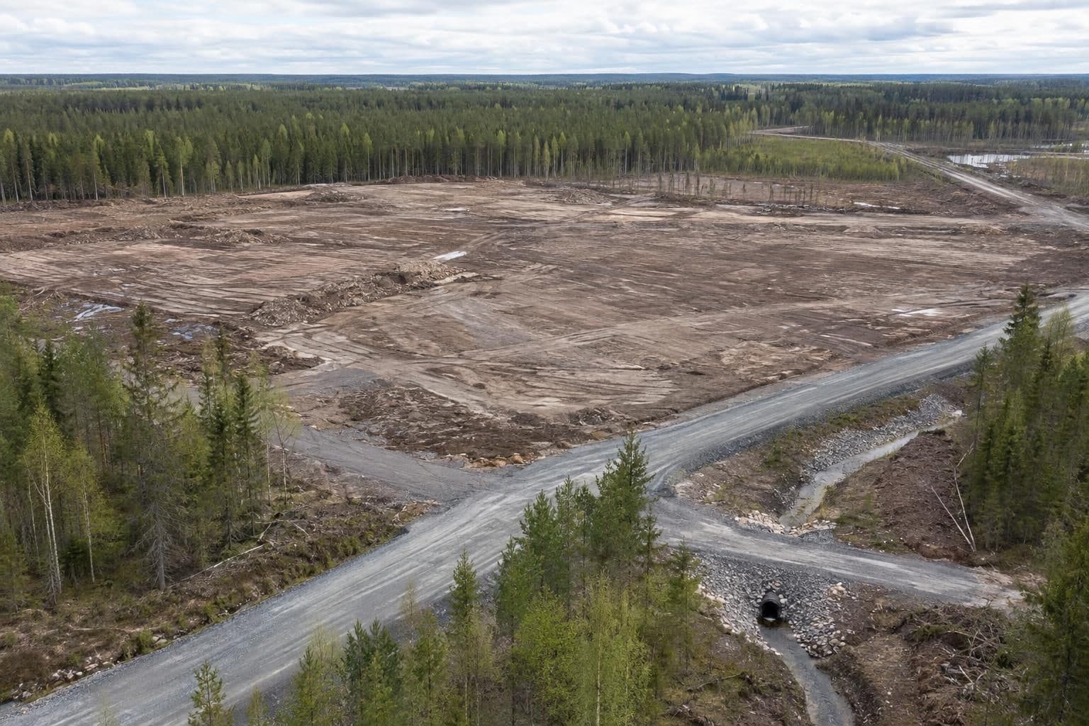 A cleared forest site shows exposed soil, a site road and a drainage ditch.