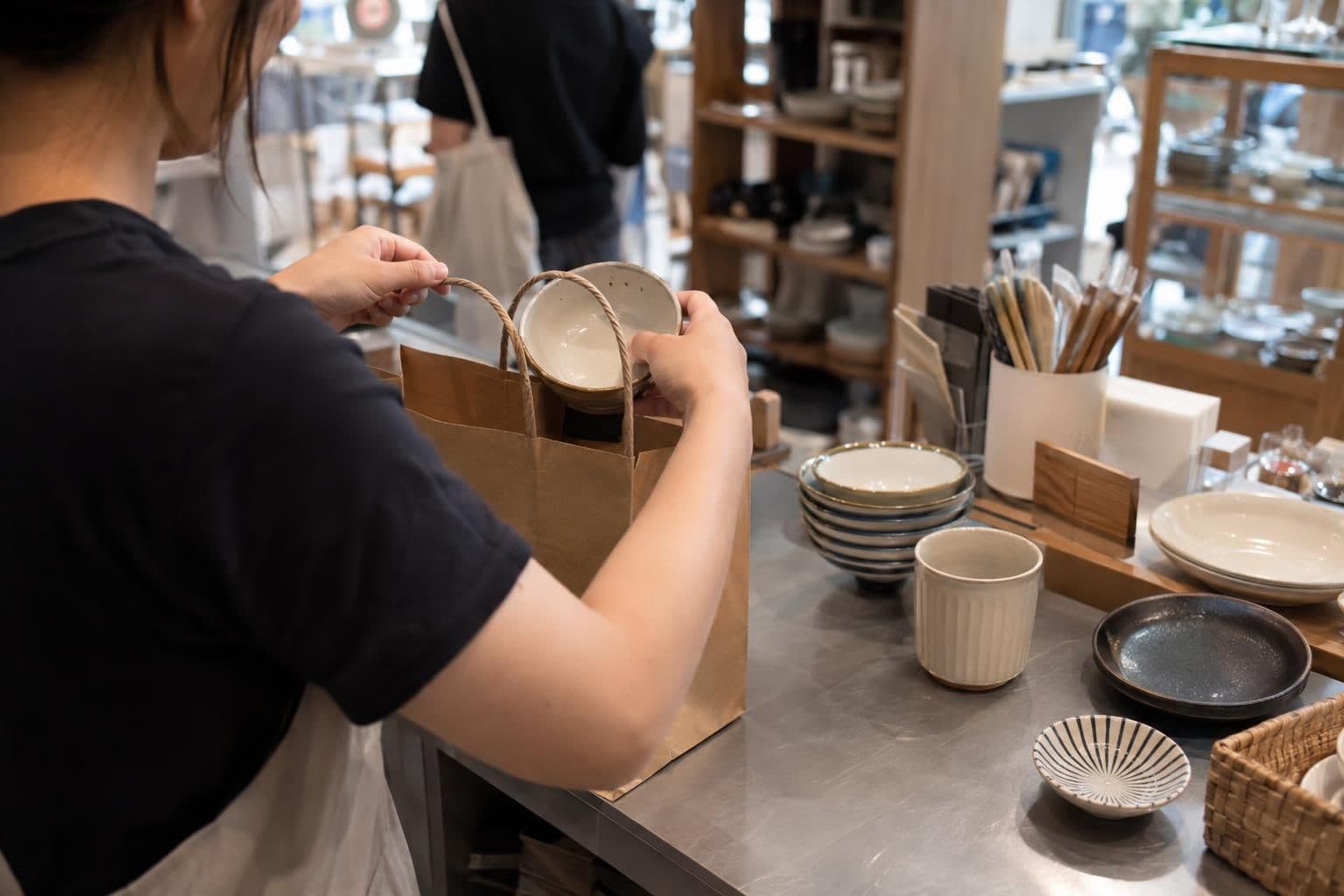 A shop worker checks items for a customer order and places them in a plain bag.