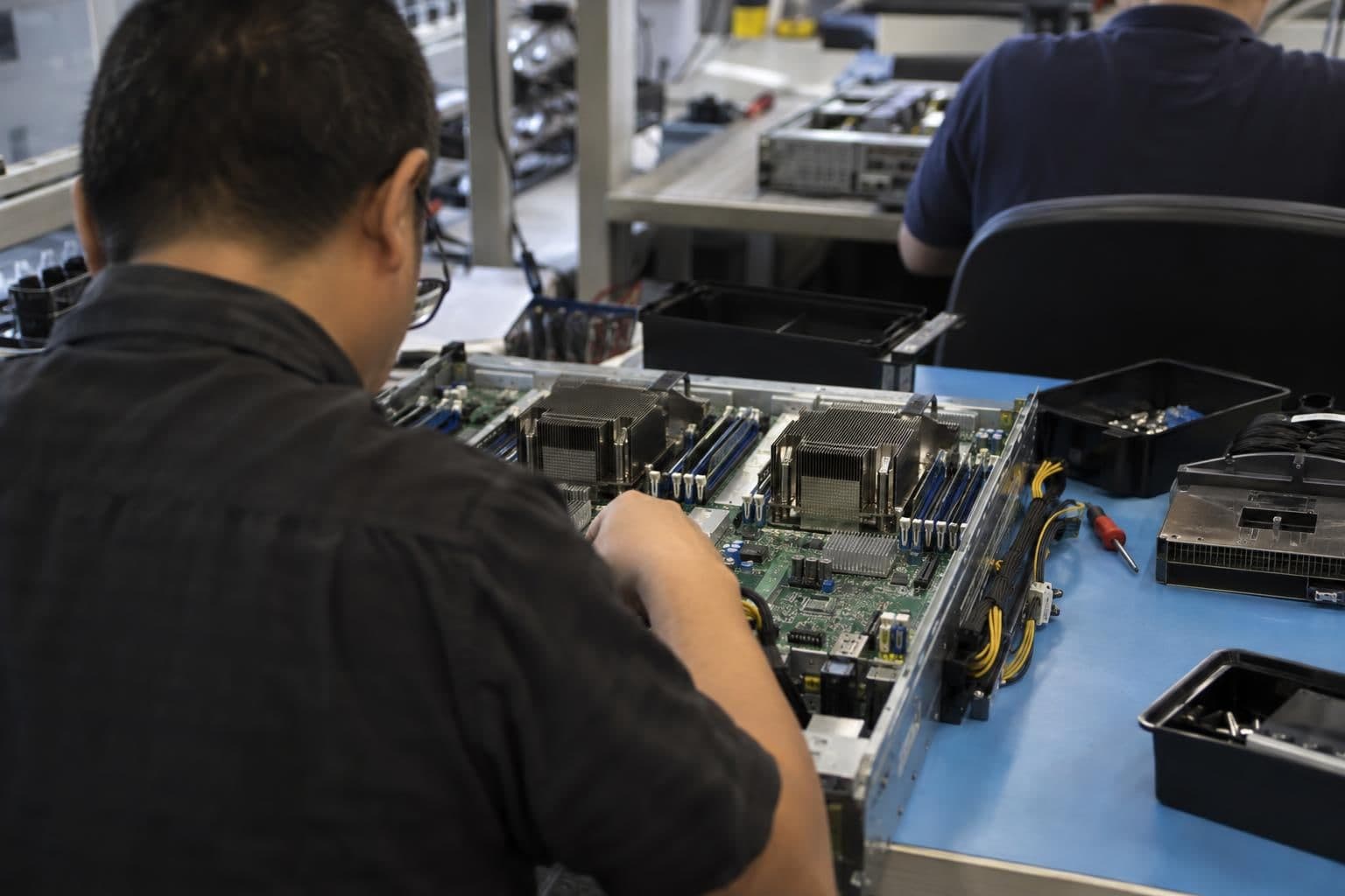Technicians inspect CPU server hardware at a development bench.