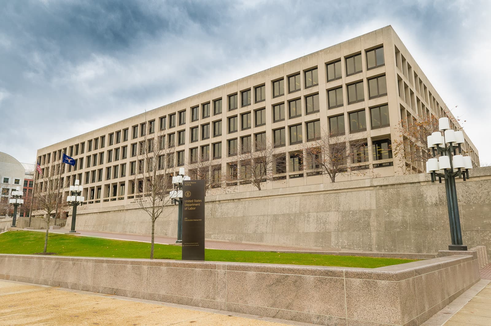 A large government office building with rows of windows behind a stone wall and lawn.